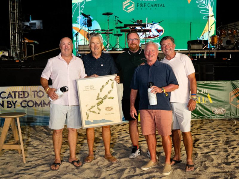 Five men stand together on the sand, holding a framed map, celebrating at the Stars & Stripes Tournament event.