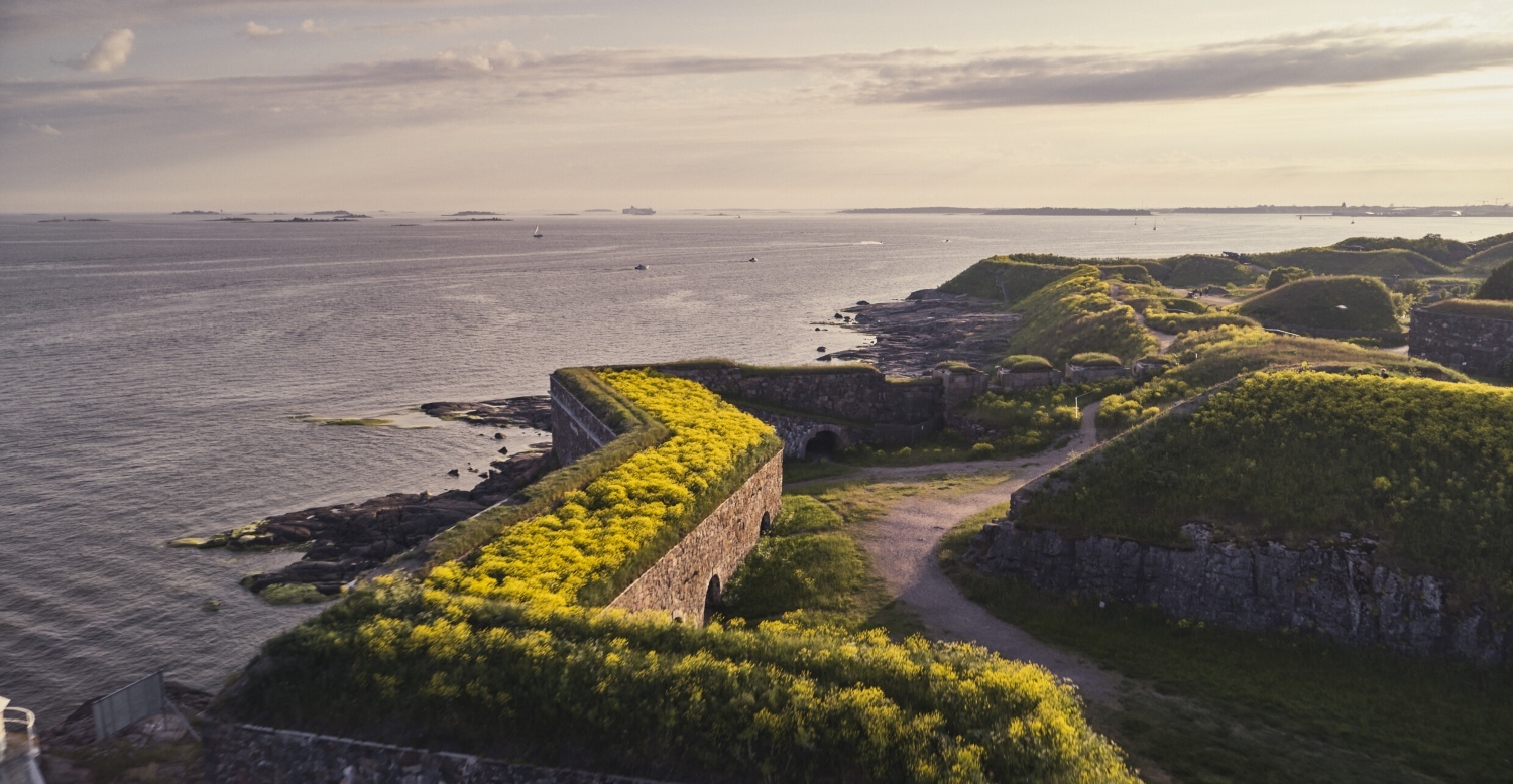 Aerial view of Suomenlinna, showcasing lush green hills and stone fortifications along the coastline.