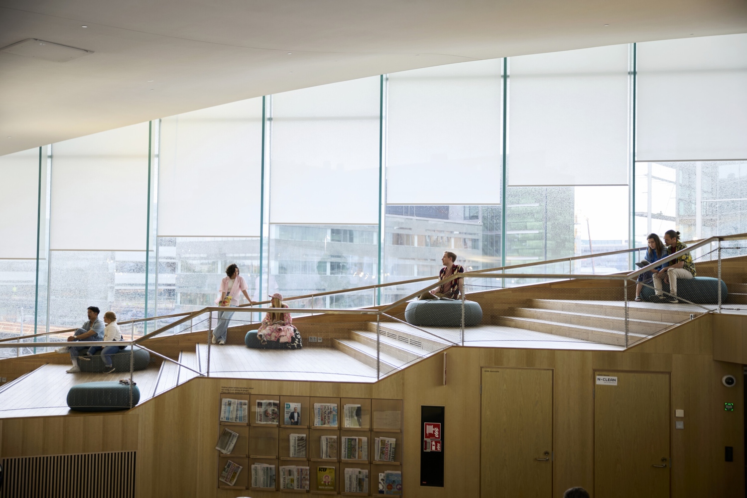 People relax and read in a modern, bright space with large windows and wooden steps, capturing the atmosphere of a community hub.