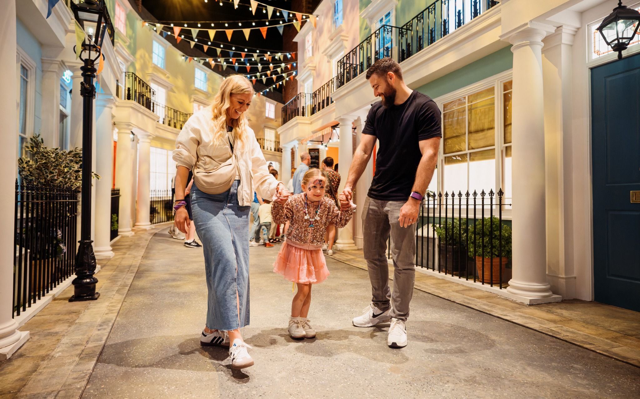 A family enjoys a lively street experience, walking hand in hand with colorful decorations in a cheerful atmosphere.