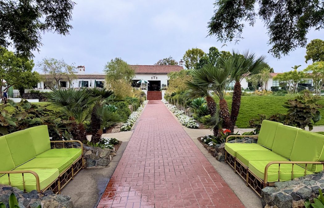 Pathway leading to The Inn at Rancho Santa Fe, lined with greenery and vibrant seating in a tranquil garden setting.