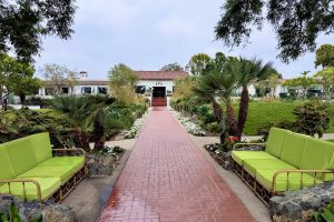 Pathway leading to The Inn at Rancho Santa Fe, lined with greenery and vibrant seating in a tranquil garden setting.