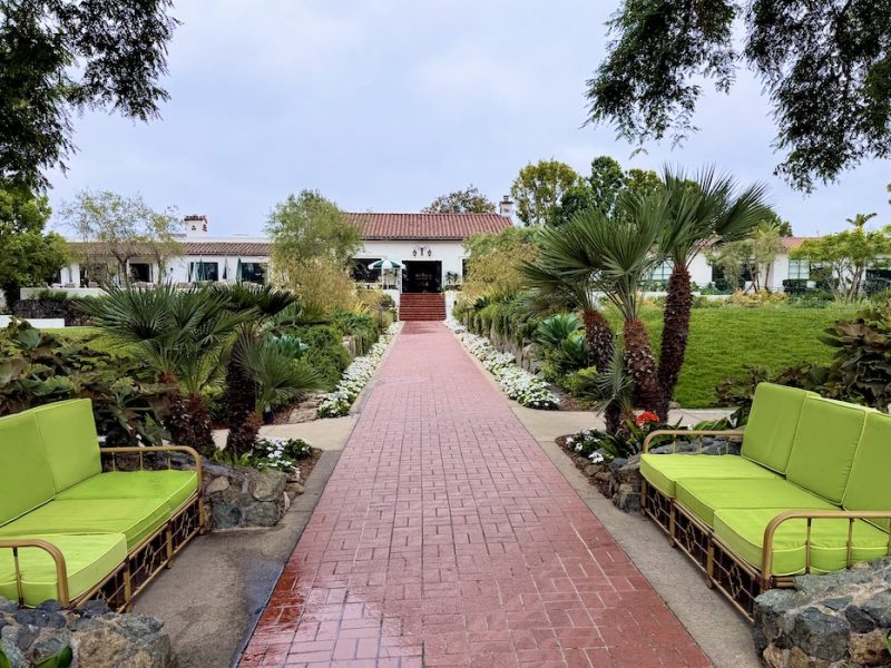 Pathway leading to The Inn at Rancho Santa Fe, lined with greenery and vibrant seating in a tranquil garden setting.