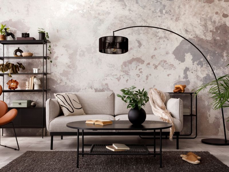 A stylish living room featuring a beige sofa, black coffee table, and decorative plants against a textured wall.