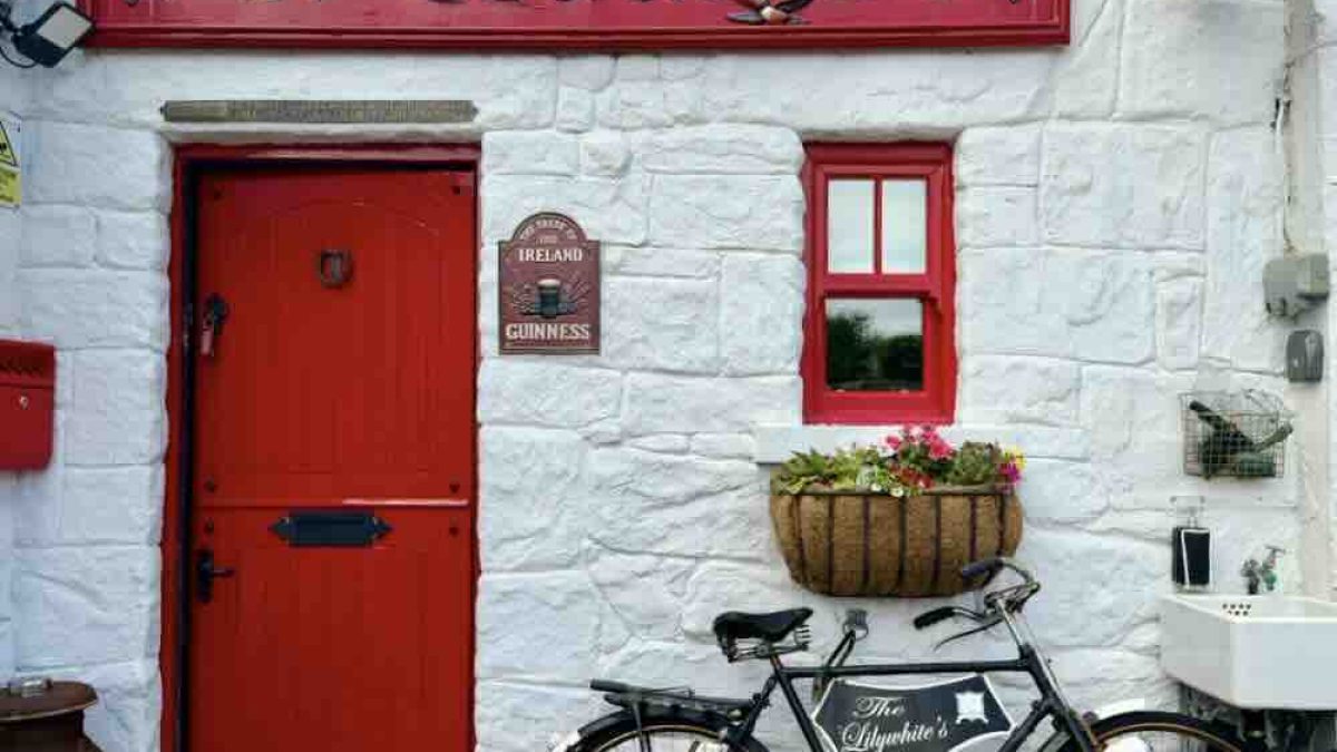 Exterior view of An Teach Bó guesthouse featuring a red door, historic artefacts, and decorative flower basket.
