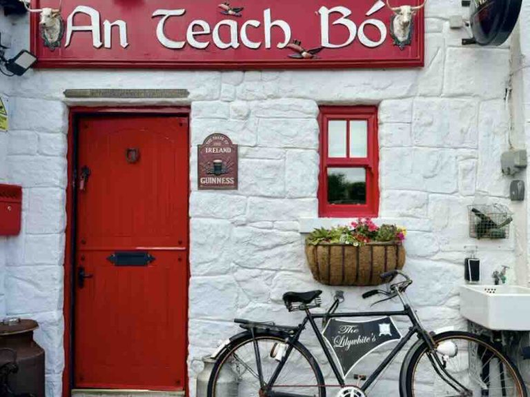 Exterior view of An Teach Bó guesthouse featuring a red door, historic artefacts, and decorative flower basket.