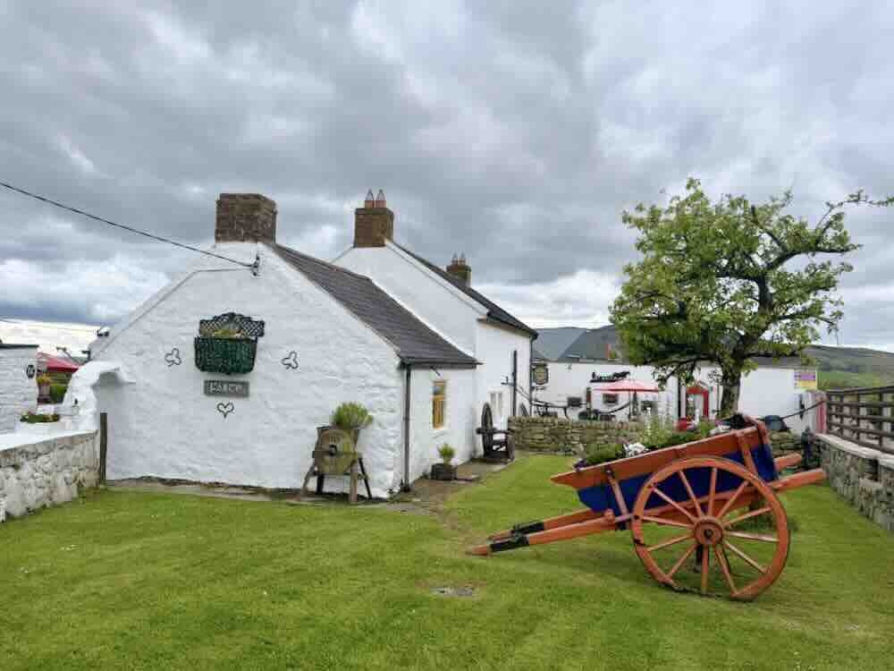 Historic Irish guesthouse with white exterior, a vintage cart, and lush green lawn under a cloudy sky.