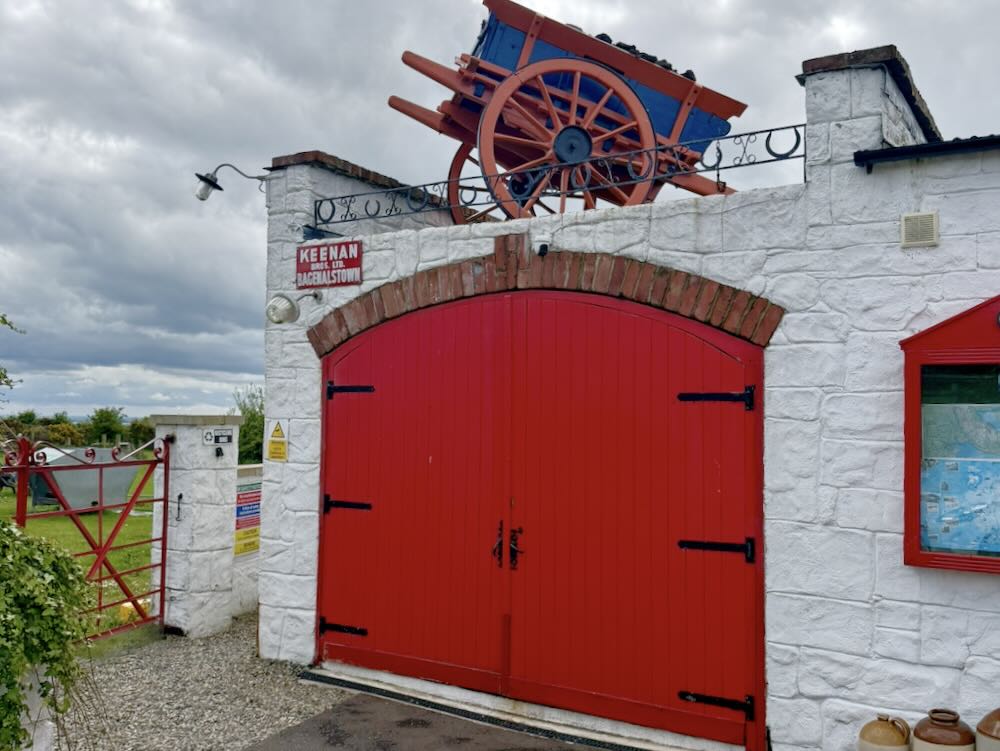 Red double doors with a historic cart atop the entrance to a luxury Irish guesthouse featuring artefacts.