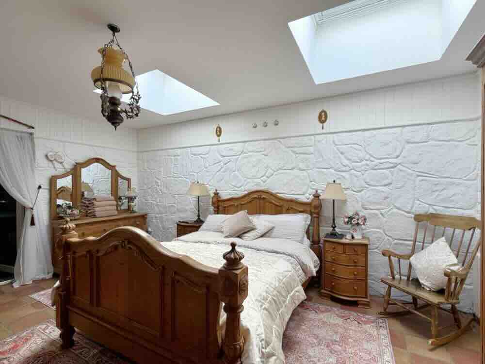 Luxurious guesthouse bedroom featuring a wooden bed, vintage decor, and natural light from skylights.