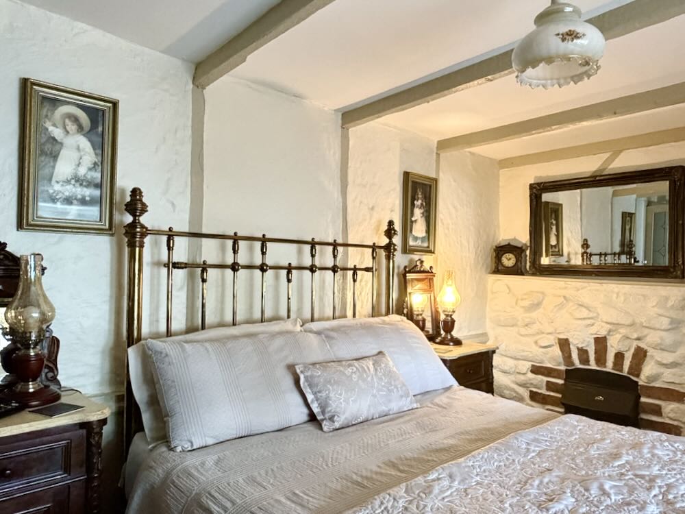 Luxurious guesthouse bedroom featuring a brass bed, antique lamps, historic artefacts, and framed portraits on the walls.