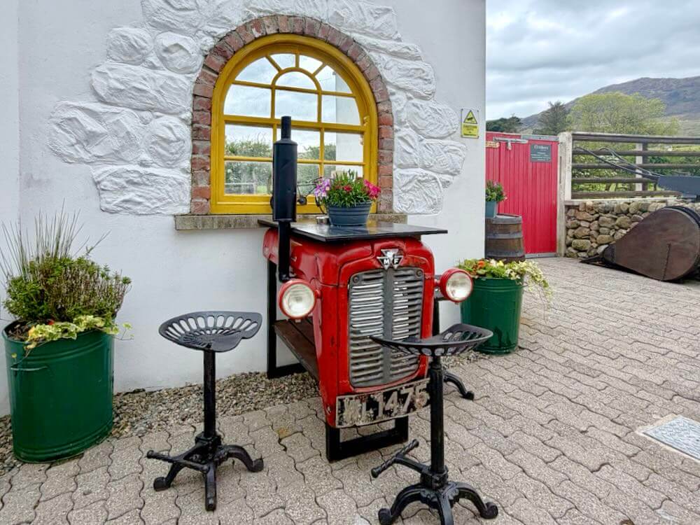 A rustic red tractor converted into a bar table with stools, surrounded by planters and a bright yellow window.