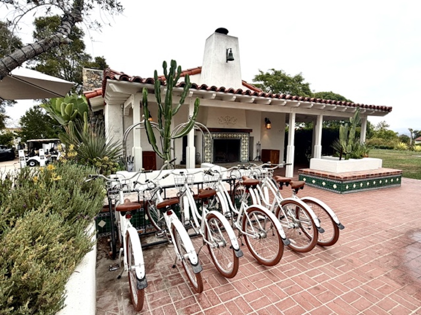 Bicycles lined up in front of a Spanish-style building with a tile fireplace and surrounding greenery at The Inn at Rancho Santa Fe.