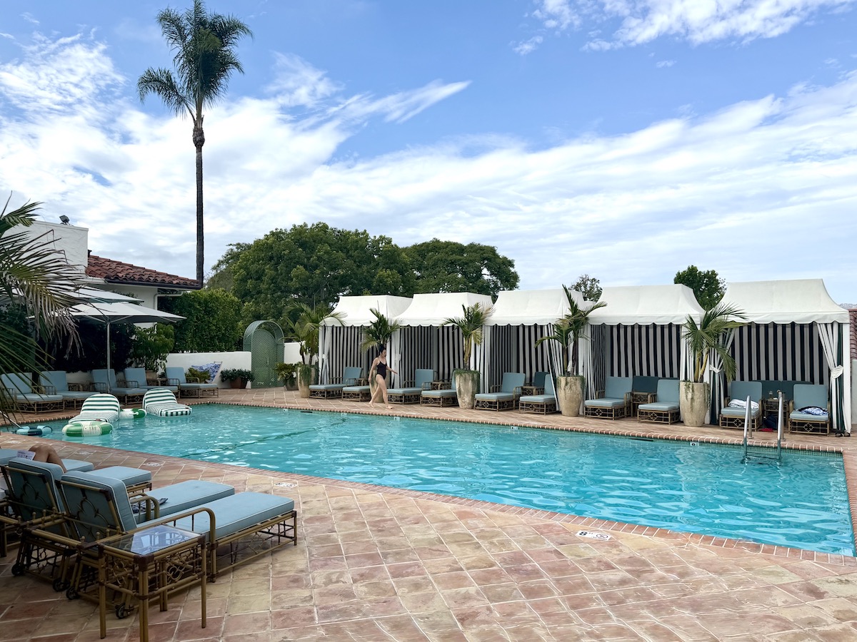 Stylish pool area at The Inn at Rancho Santa Fe, featuring cabanas, lounge chairs, and tropical plants under a blue sky.