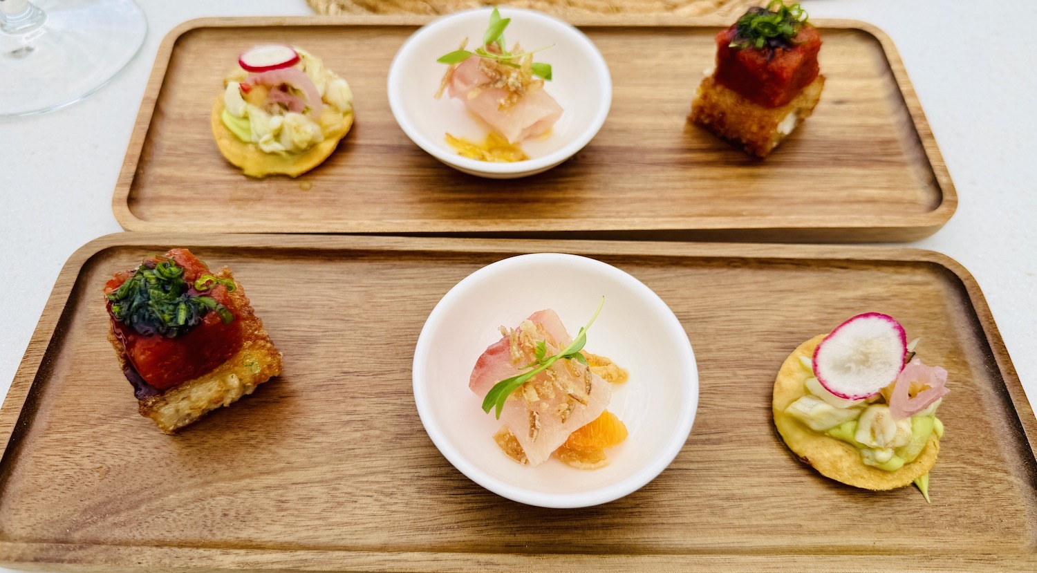 Elegant amuse-bouche consisting of small bites on wooden trays, featuring fresh ingredients and colorful garnishes.