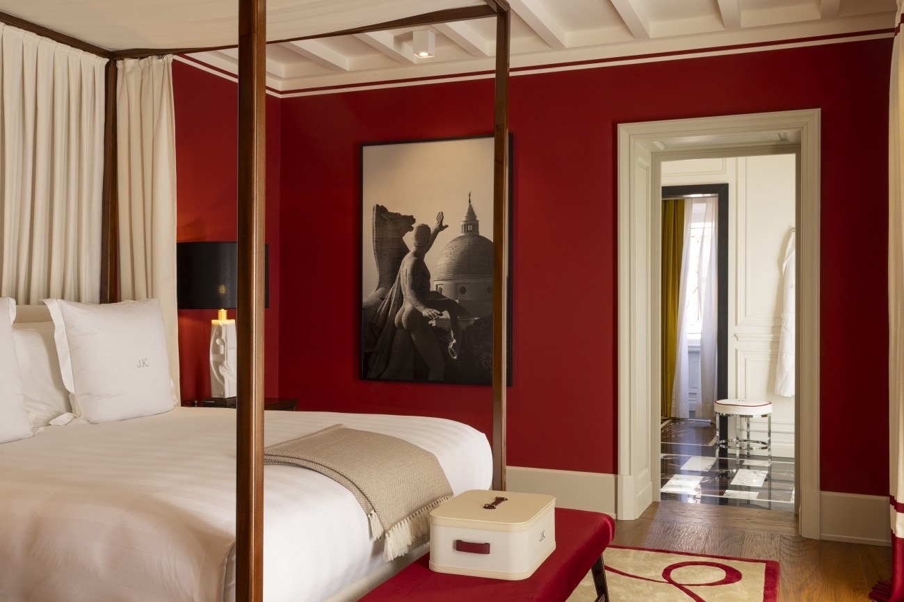 Stylish hotel room featuring a red accent wall, a four-poster bed, artwork, and a view of the doorway to a modern bathroom.