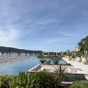 Lazure Hotel & Marina features a serene poolside view overlooking a beach with lounge chairs and a mountainous backdrop.