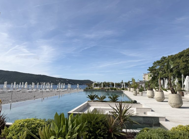 Lazure Hotel & Marina features a serene poolside view overlooking a beach with lounge chairs and a mountainous backdrop.