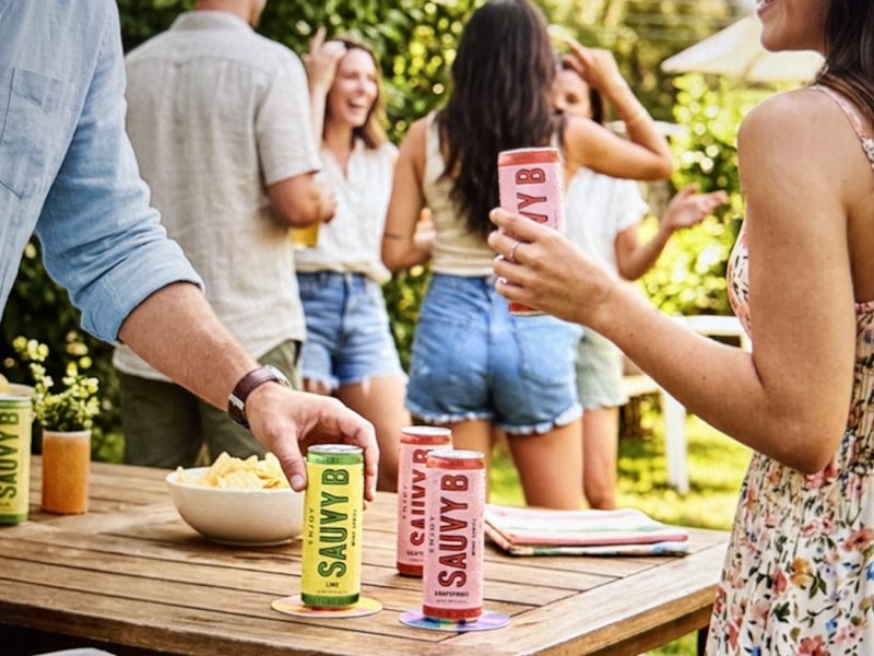People enjoying a lively outdoor gathering while holding cans of Sauvy B, a Sauvignon Blanc spritz with electrolytes.