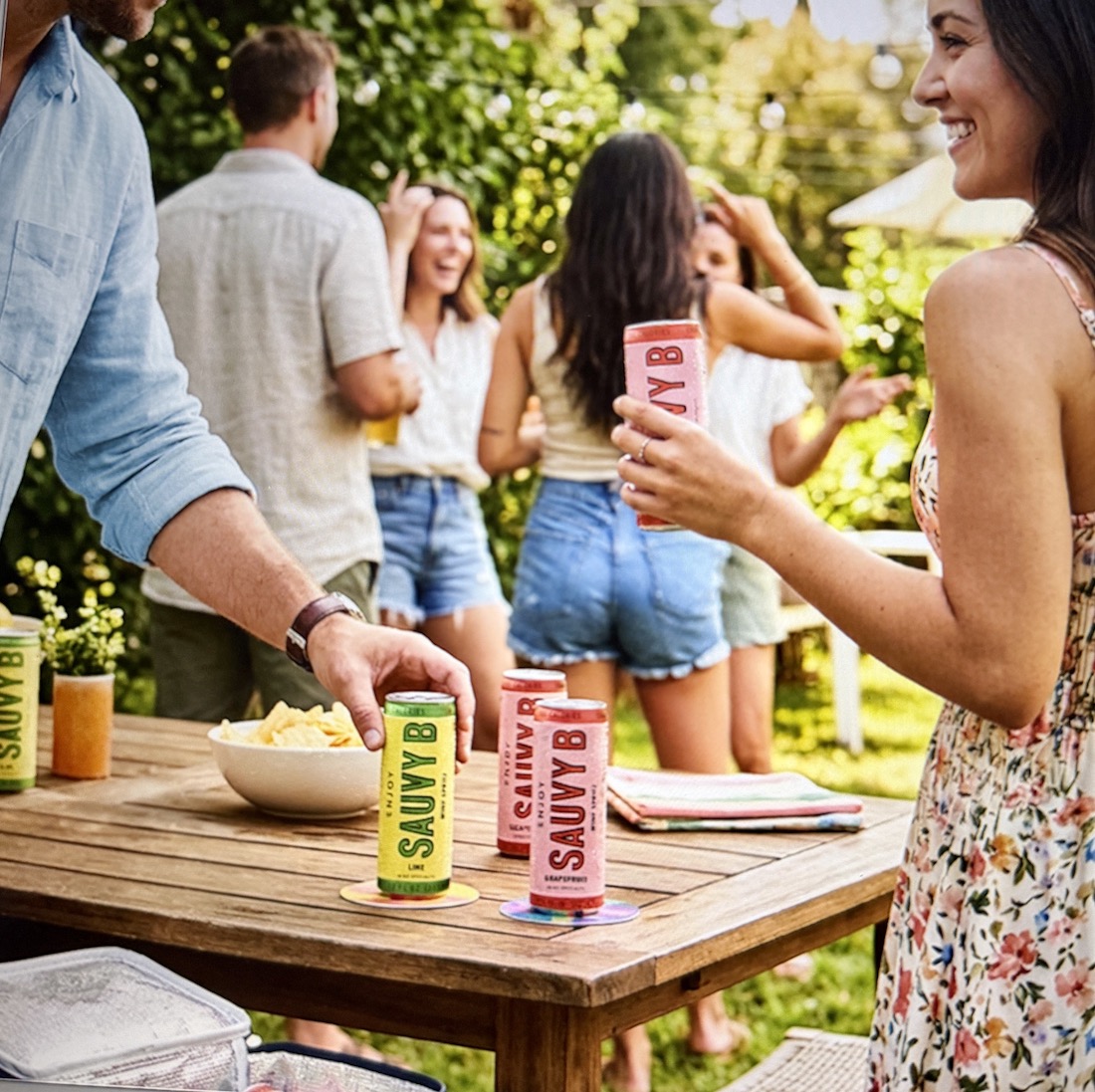 People enjoying a lively outdoor gathering while holding cans of Sauvy B, a Sauvignon Blanc spritz with electrolytes.