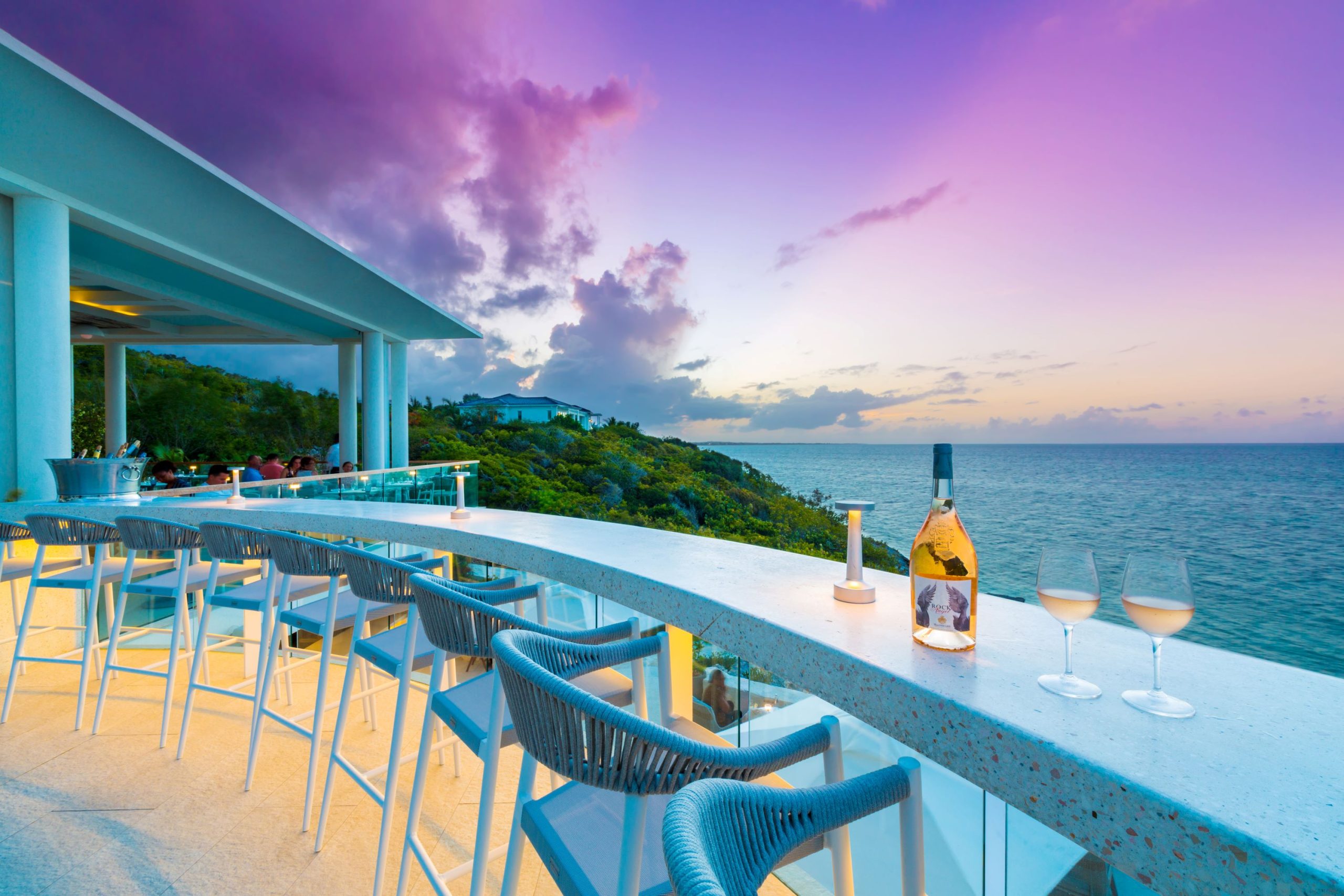 A stylish bar setup overlooking the ocean at sunset, complete with drinks and a vibrant sky in Turks and Caicos.