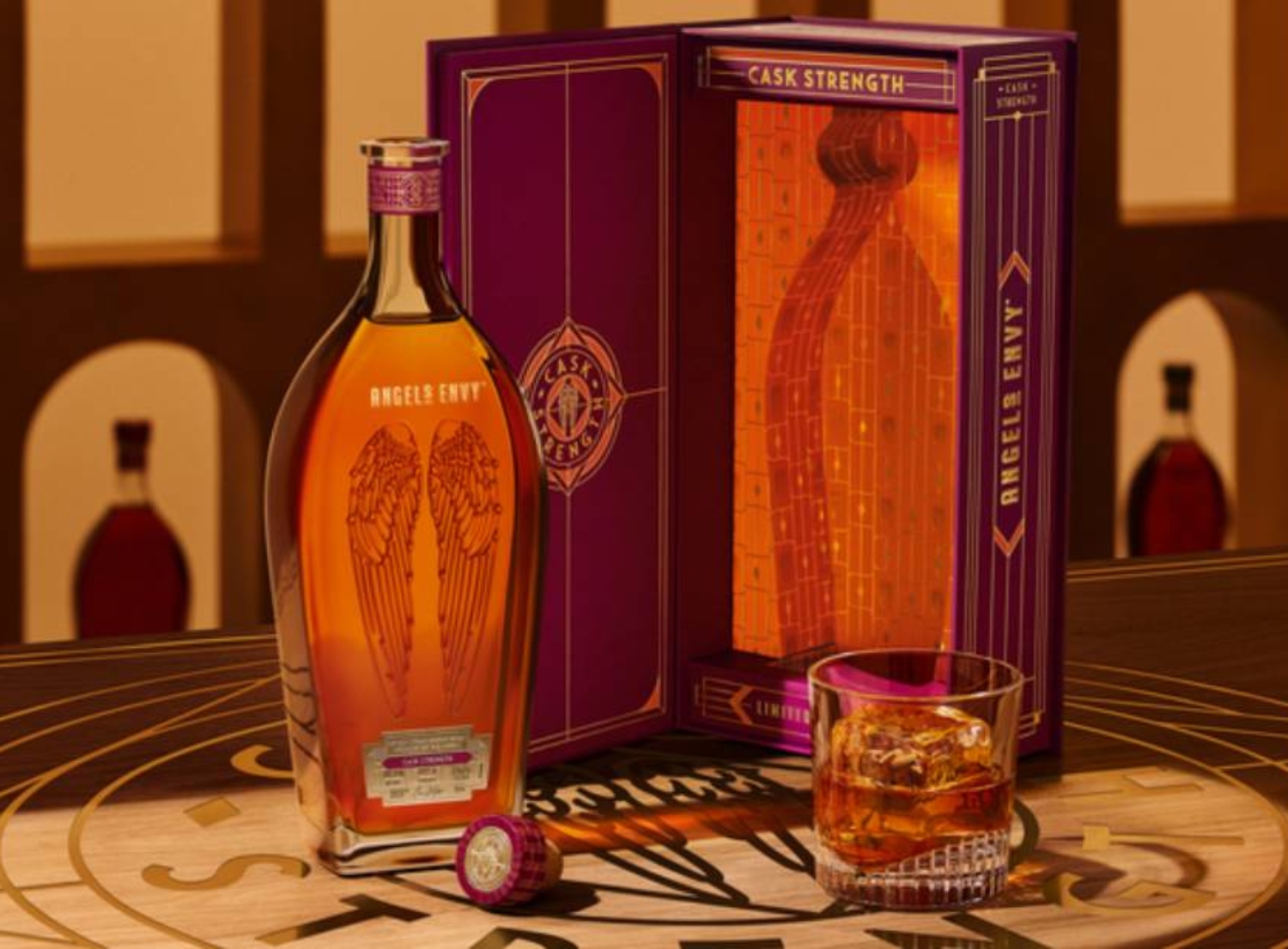 Angels Envy cask strength whiskey bottle next to a glass with whiskey and ice, displayed on a wooden table.