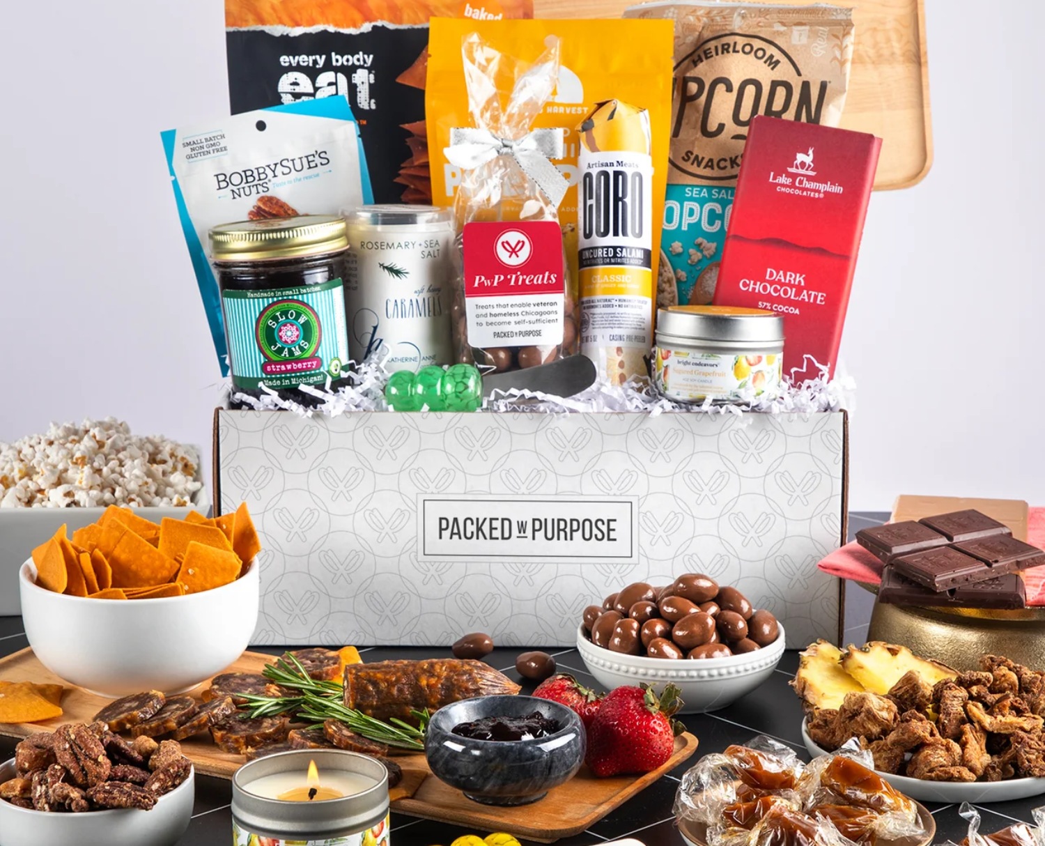 An assortment of snacks and treats arranged in a box, featuring nuts, chocolates, popcorn, and gourmet items for a festive occasion.