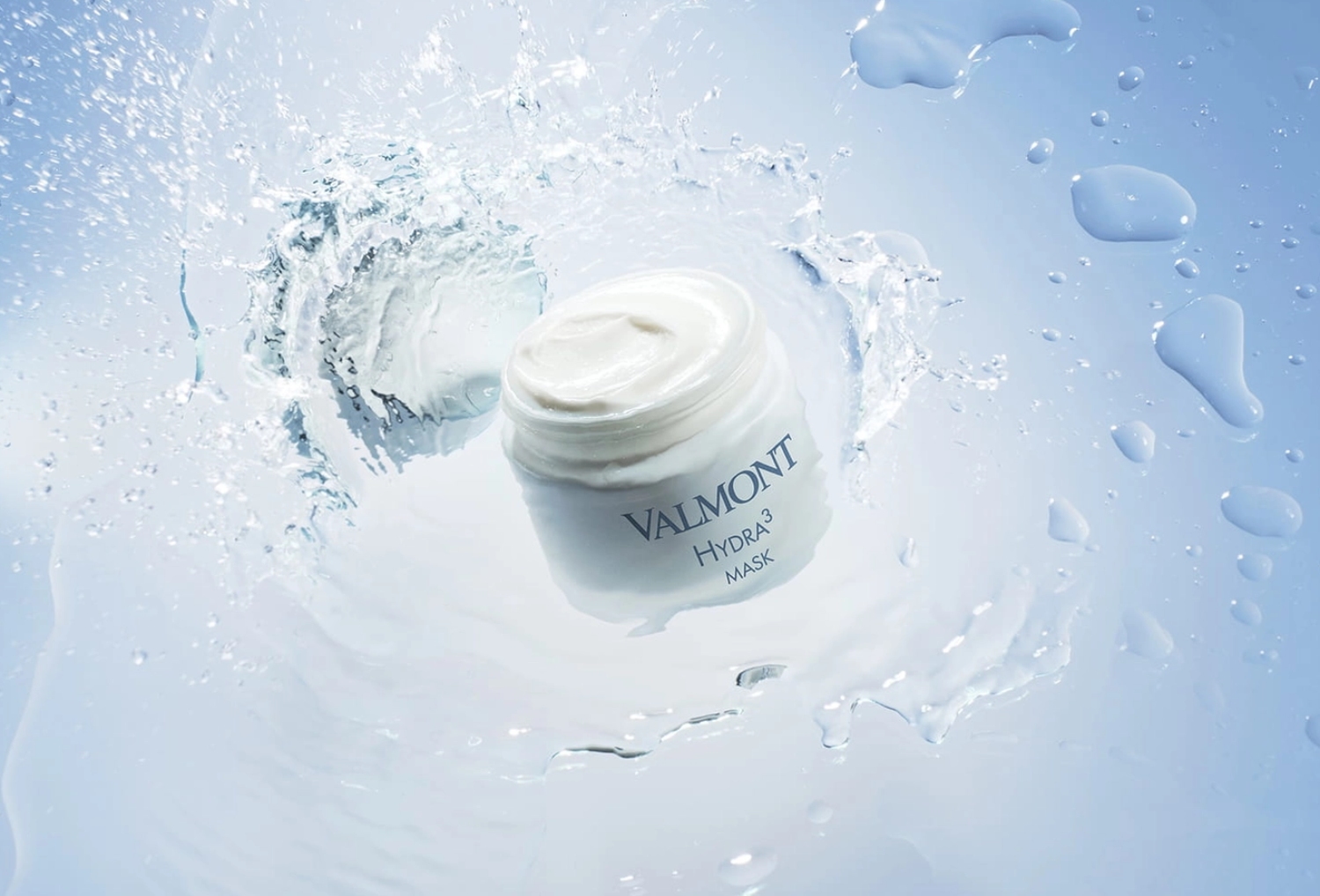 Valmont Hydra 3 mask jar surrounded by splashes of water against a soft blue background.