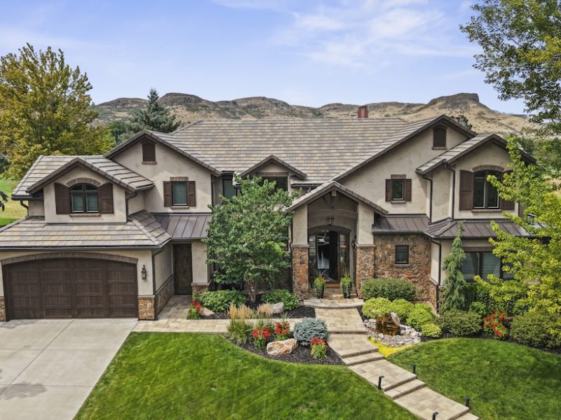 Exterior view of a spacious house surrounded by lush landscaping and mountains in the background, offering a stunning golf course address.