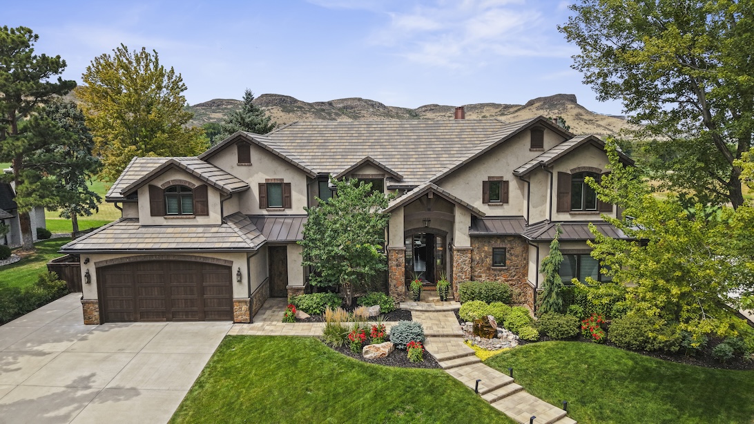 Exterior view of a spacious house surrounded by lush landscaping and mountains in the background, offering a stunning golf course address.