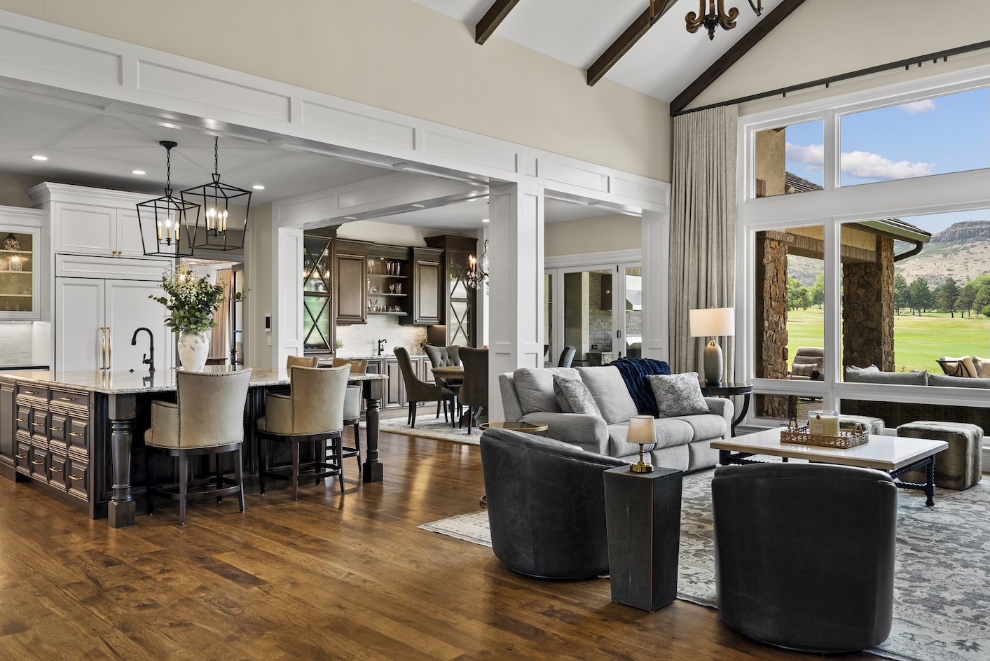Bright, open living space with a modern kitchen, elegant furnishings, and views of the golf course and mountains beyond.