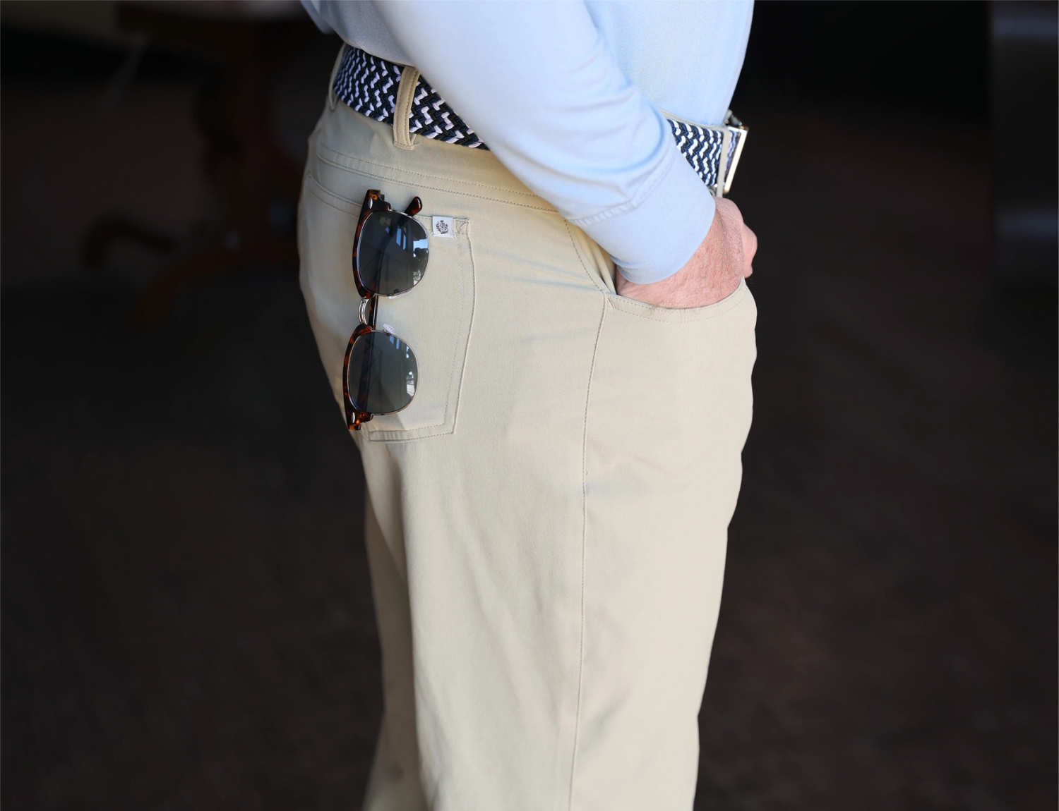 Light-colored pants with sunglasses hanging from the back pocket and a patterned belt, styled for a relaxed look.