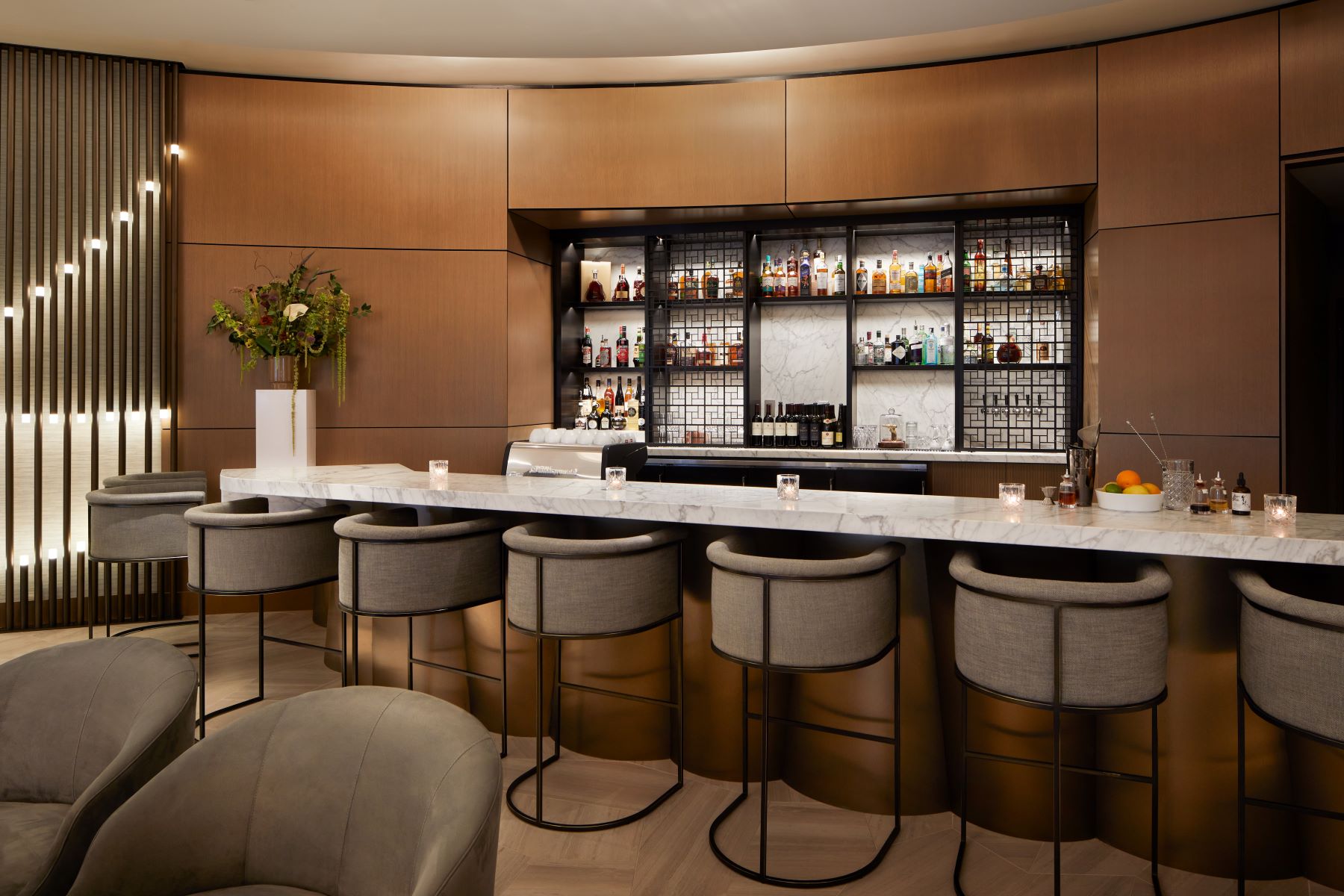 Elegant bar area featuring a marble counter, modern stools, and a well-stocked shelf of fine spirits and decorative elements.