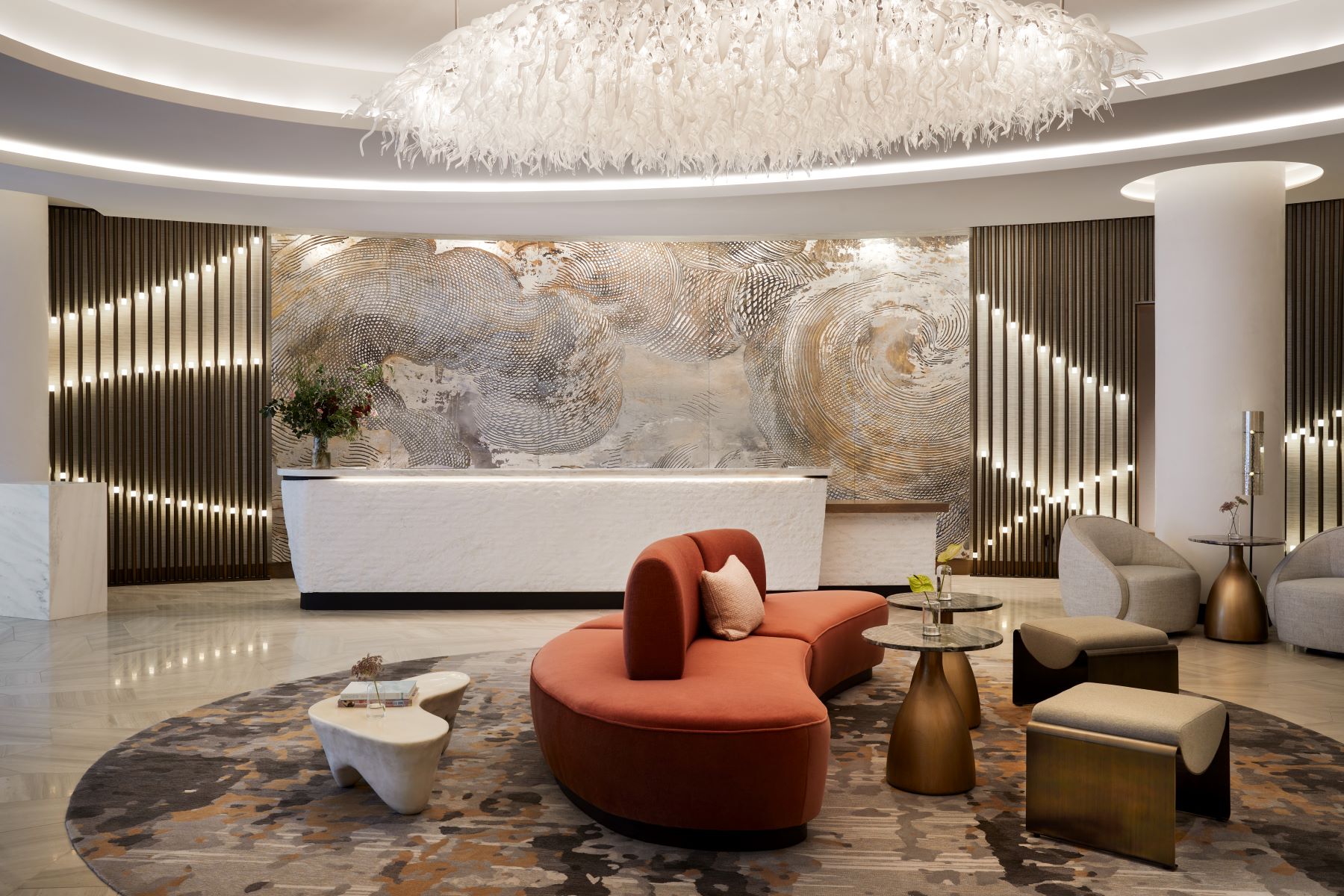 Modern hotel lobby featuring a curved orange sofa, artistic wall decor, and stylish lighting elements.