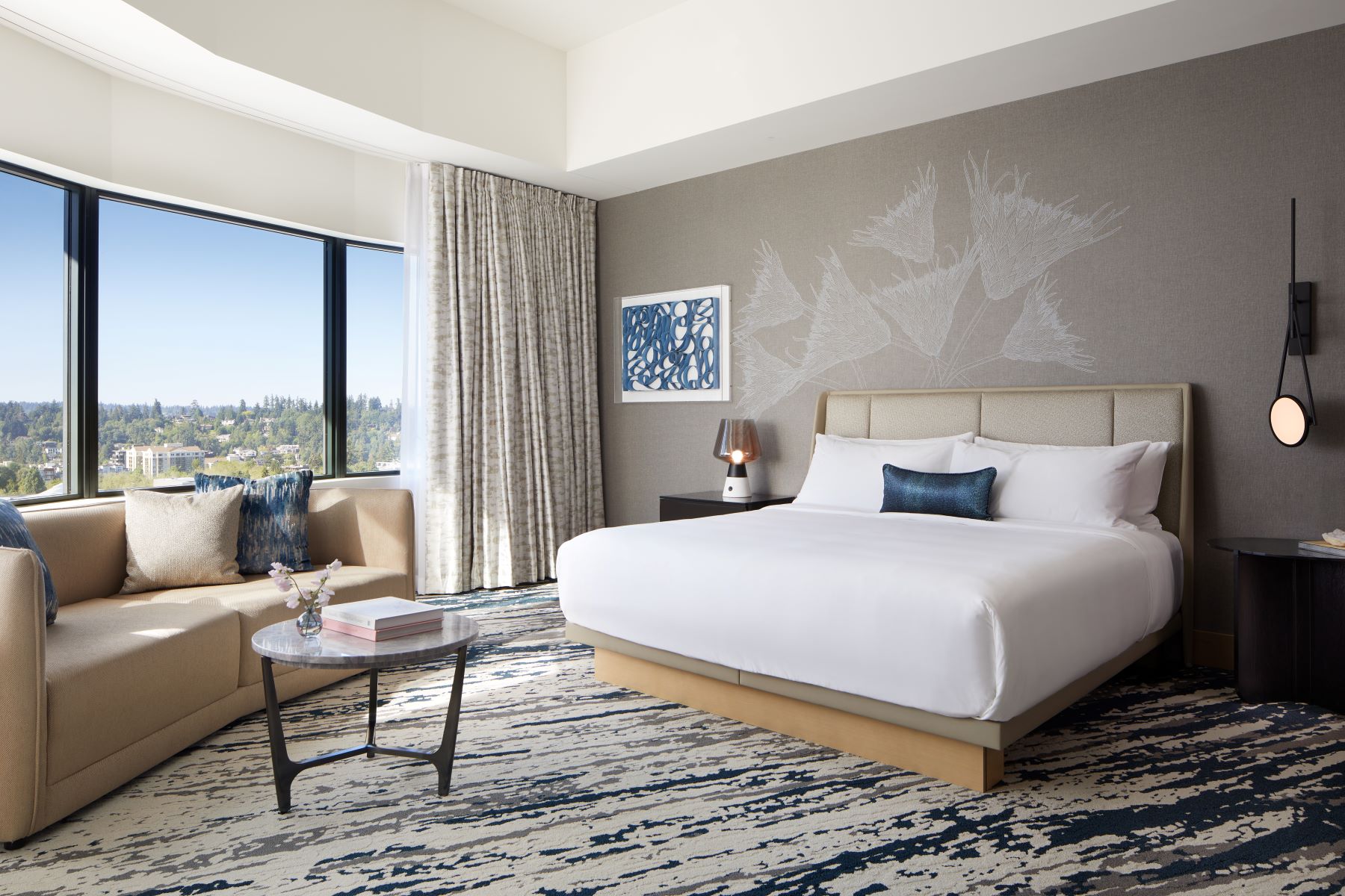 Stylish hotel room featuring a queen bed, seating area, large windows with views, and modern decor elements.