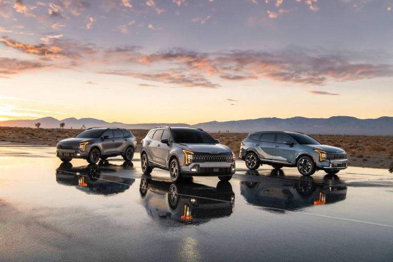 Three Kia SUVs are parked on a reflective surface at sunset, showcasing their sleek designs against a desert backdrop.