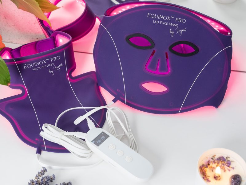 LED face mask and neck treatment by Equinox, featuring purple design with glowing lights, control remote, and relaxing ambiance.