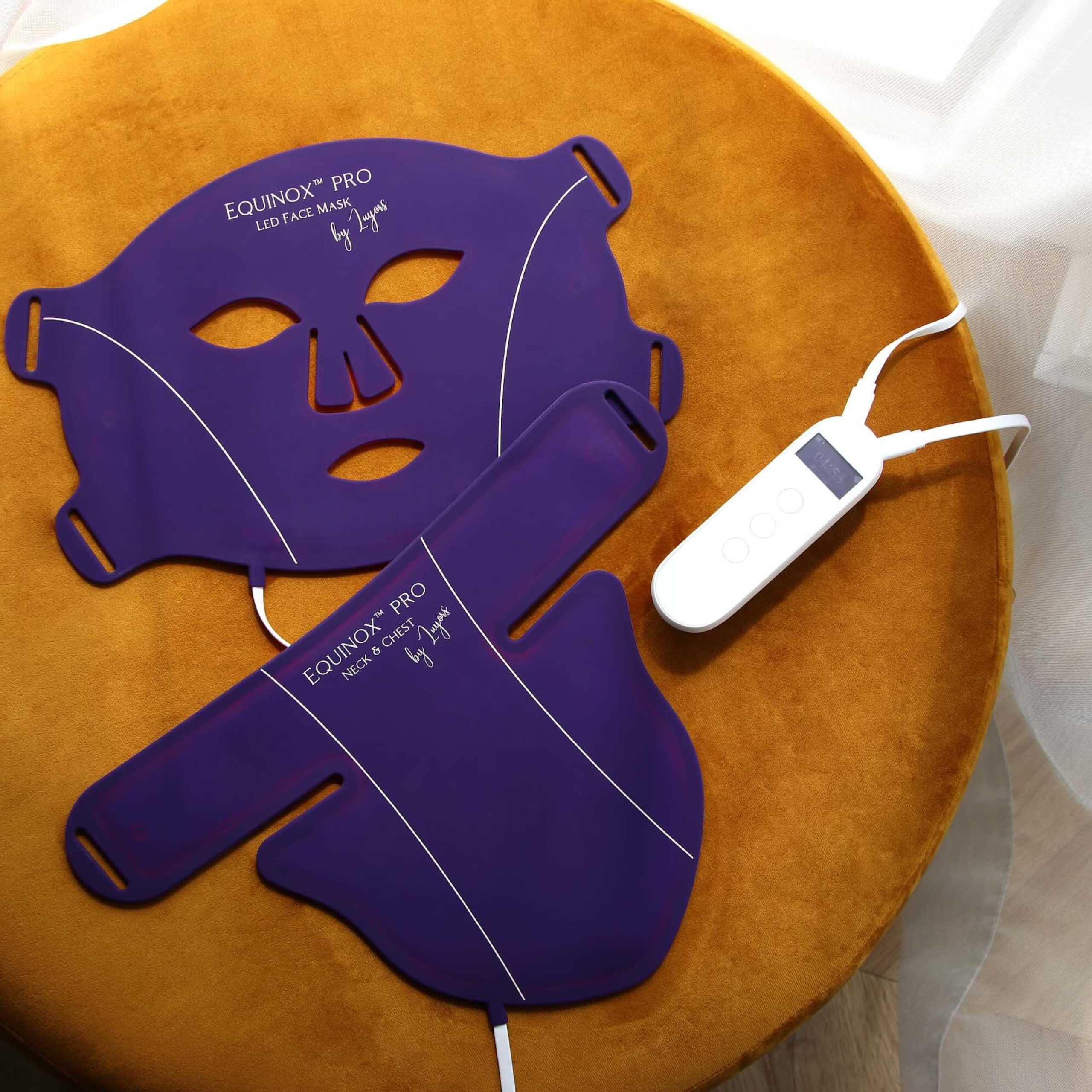 Purple LED face mask and controller placed on a round, orange velvet ottoman, promoting at-home light therapy experiences.