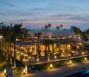 Modern dockside restaurant with outdoor seating, illuminated at dusk, surrounded by palm trees in Turks and Caicos.