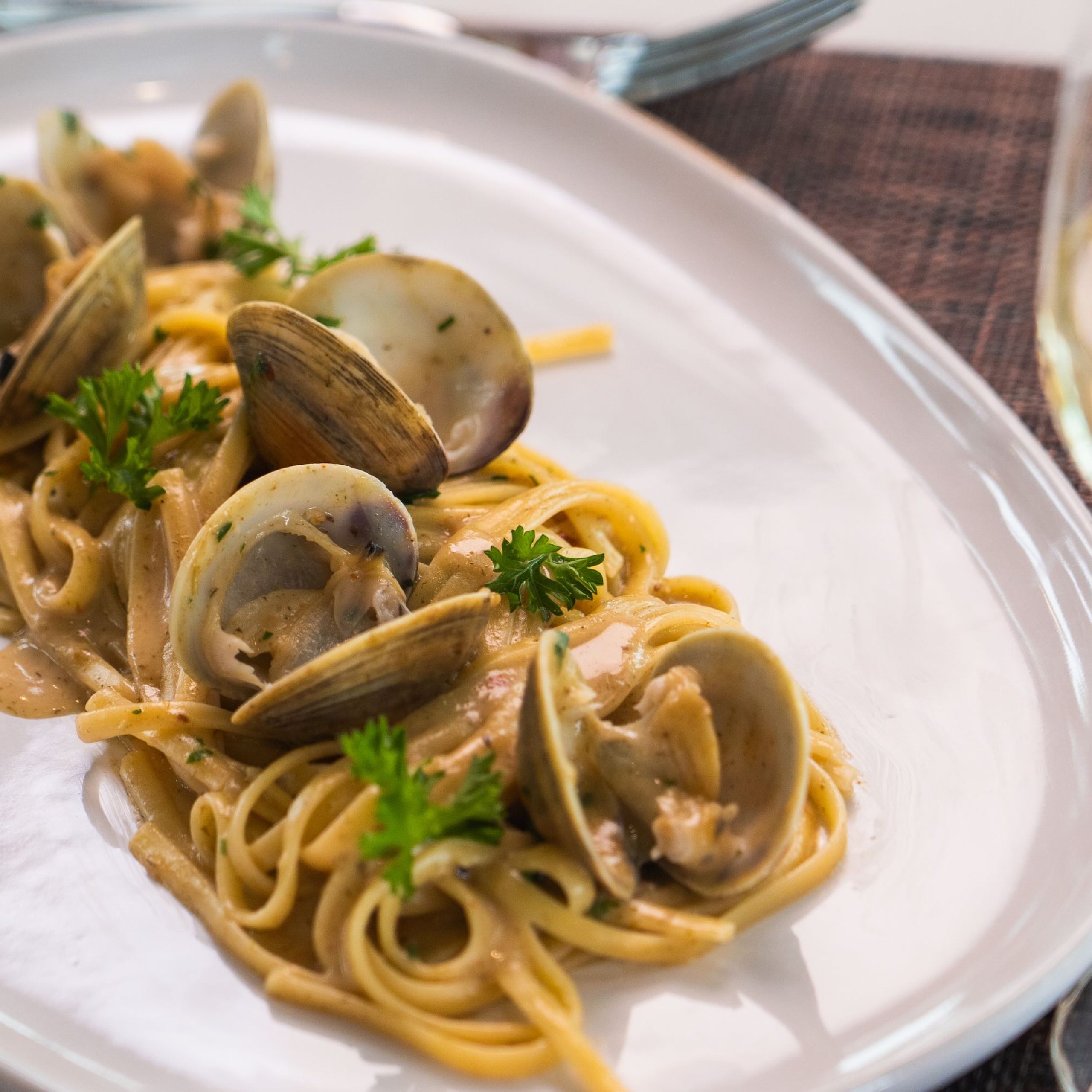 Linguine pasta with clams and herbs served on a white plate, alongside a glass of white wine.