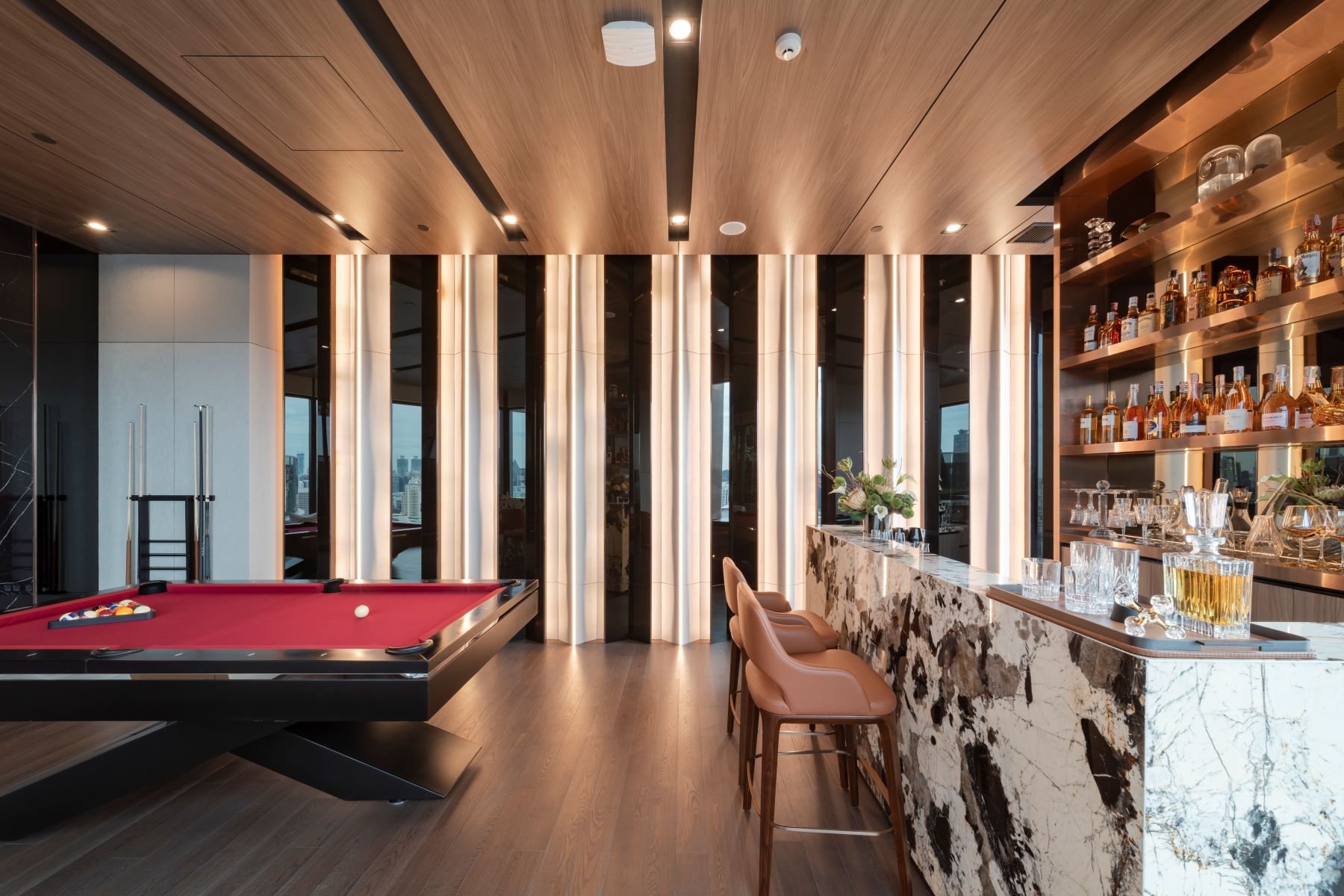 Sophisticated game room featuring a red pool table, stylish bar, and floor-to-ceiling windows offering a city view.