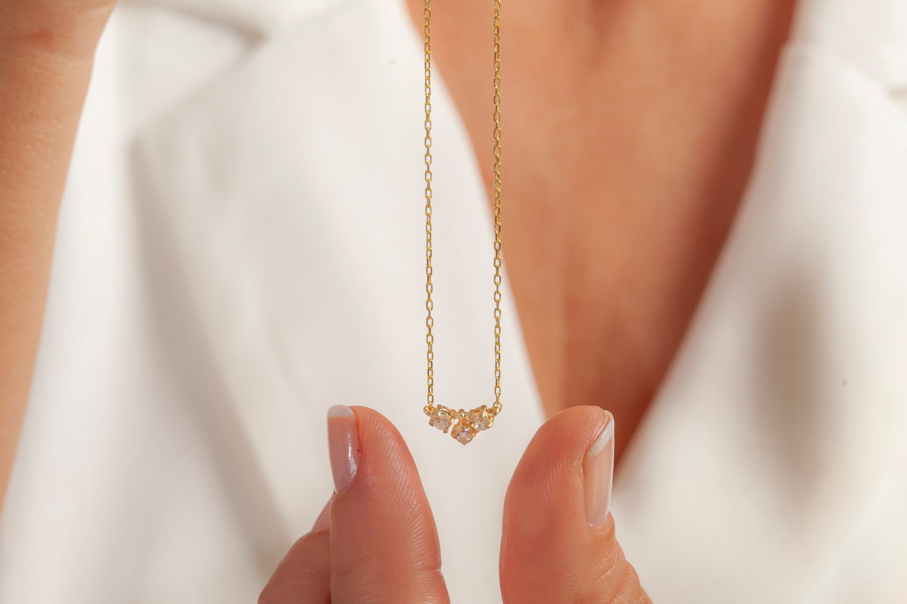A woman holds a delicate 14k gold necklace featuring three small gemstones, suitable for everyday wear.