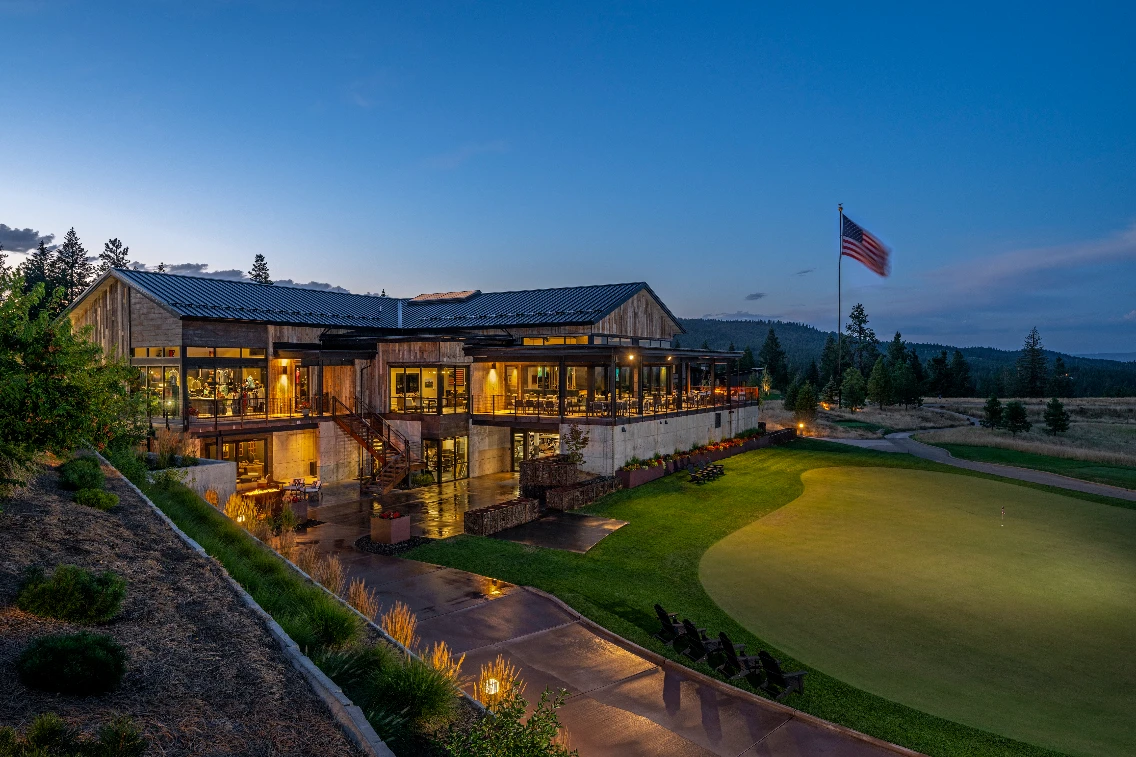 The clubhouse at CDA National Reserve illuminated at dusk, showcasing a welcoming atmosphere and scenic golf course views.