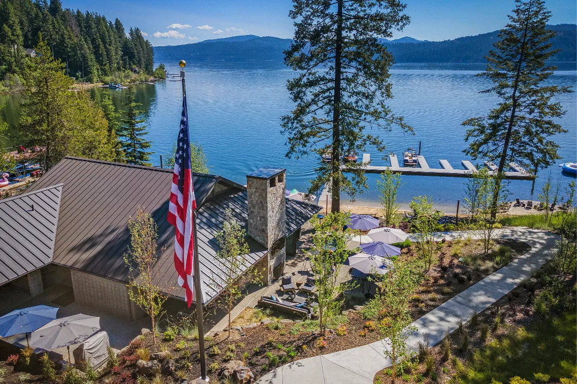 View of a lakeside property featuring a dock, a flag, and outdoor seating among trees at CDA National Reserve.