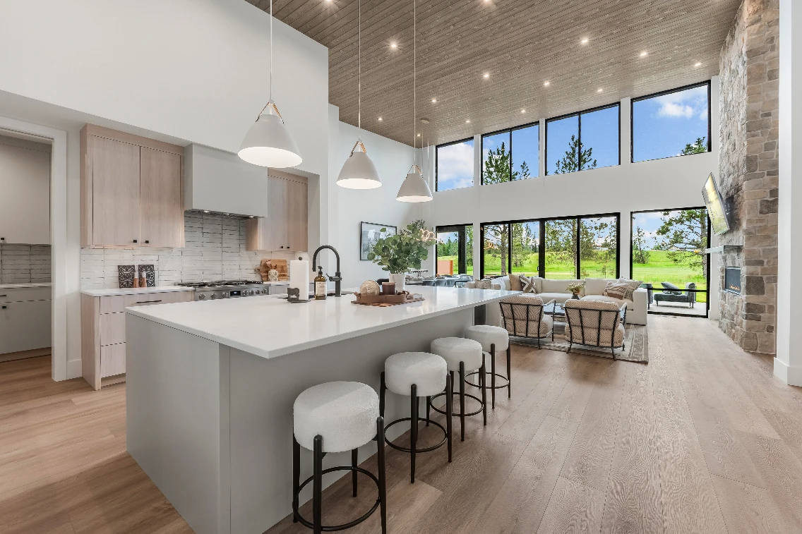 Bright and modern kitchen with a large island and seating, featuring tall windows that offer views of the outdoor landscape.