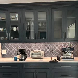 Modern kitchen cabinetry with glass doors, coffee maker, espresso machine, and neutral tile backsplash.