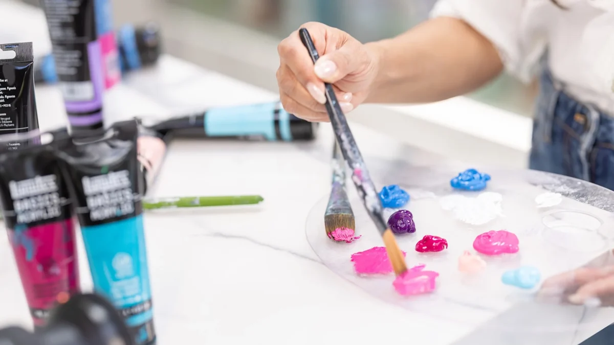 A hand selecting vibrant paint colors from a palette while preparing to create art at a studio workspace.