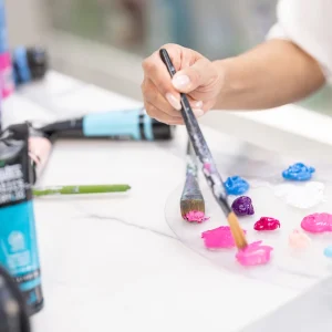 A hand selecting vibrant paint colors from a palette while preparing to create art at a studio workspace.