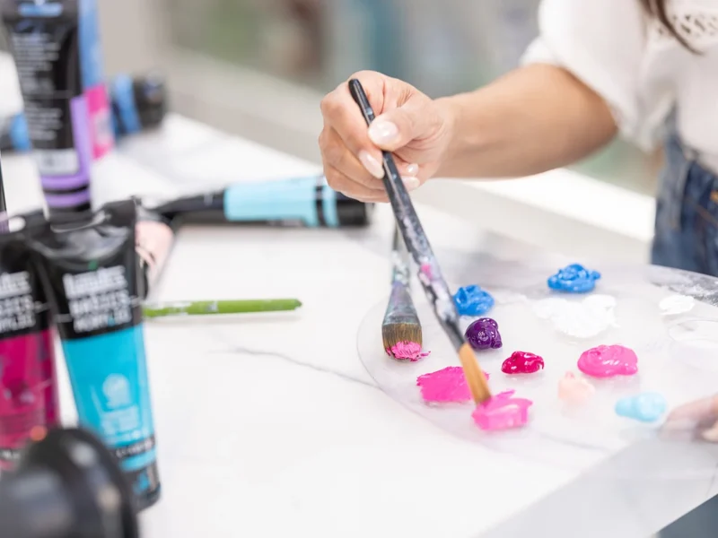 A hand selecting vibrant paint colors from a palette while preparing to create art at a studio workspace.