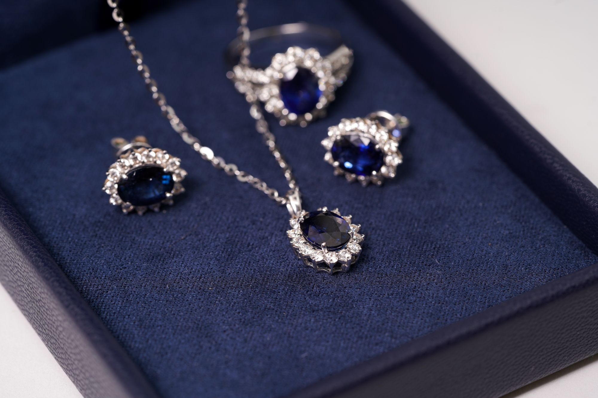 Elegant silver jewelry set featuring a necklace, earrings, and a ring with dark blue gemstones displayed on a navy background.