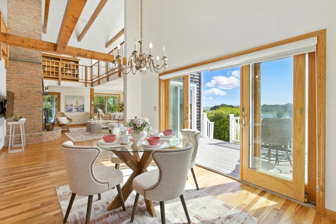 Cozy dining area with water views, featuring a round table, elegant chairs, and large glass doors leading to the deck.
